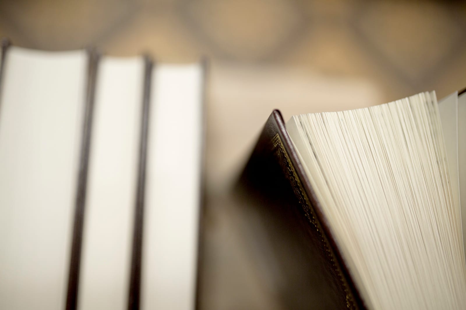 Close-up de páginas de um livro aberto ao lado de uma pilha de livros fechados de capa clara.
