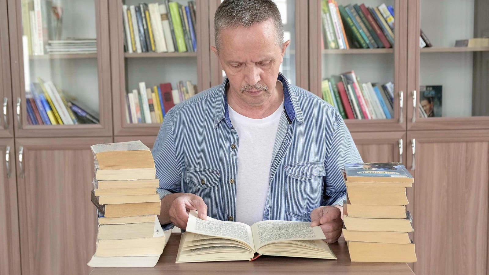 Homem sorrindo enquanto lê um livro aberto, segurando um café, em um ambiente com tijolo aparente.